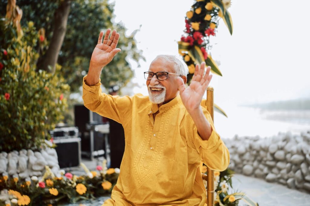 pexels photo 33885297 Happy senior man in traditional attire celebrating outdoors with lifted hands and a bright smile.