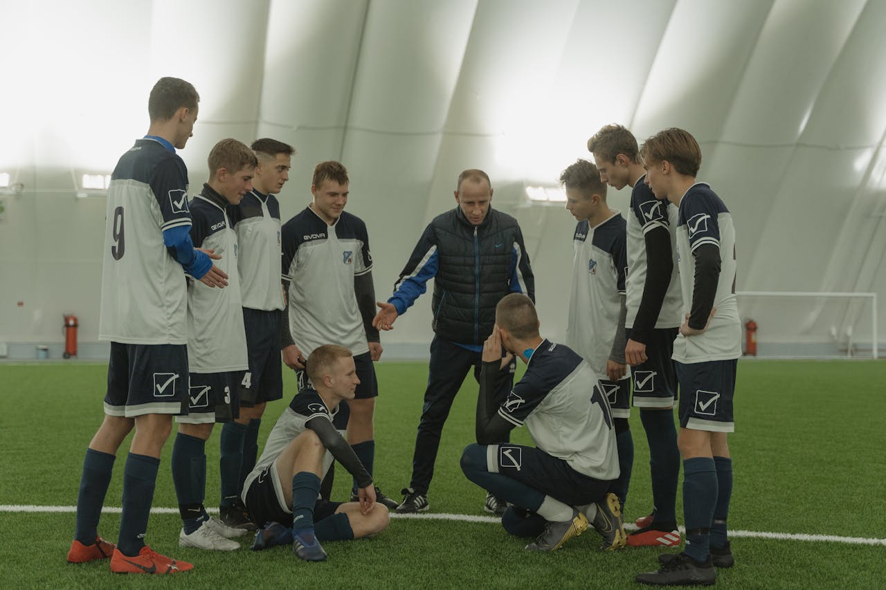 about-img A soccer coach gives tactical advice to a youth team indoors on artificial turf.