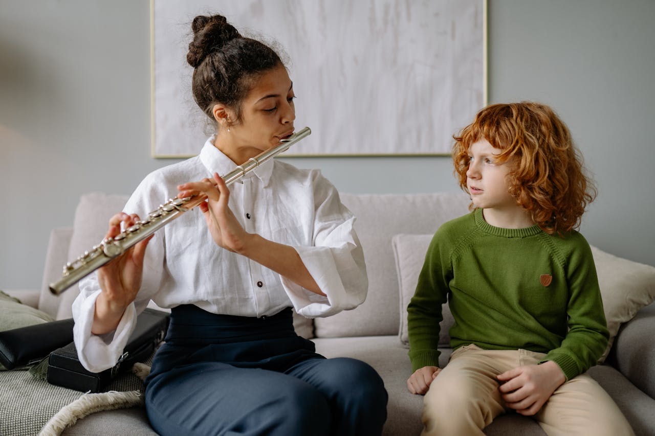 our-mission A woman teaching a child to play the flute on a sofa during a music lesson indoors.